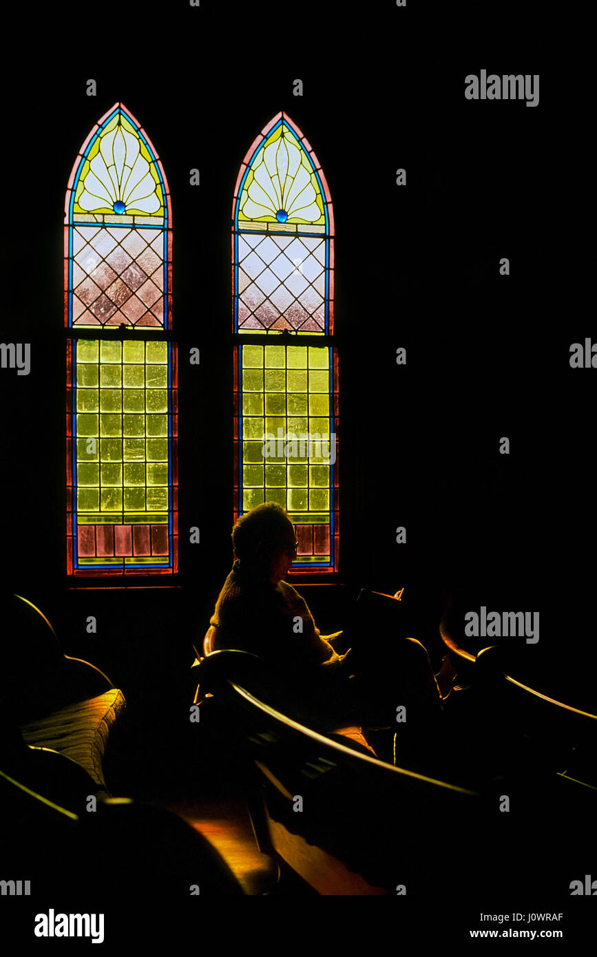 An senior man sits in church under stained glass windows reading his bible in White River Junction, Vermont, United States. Stock Photo