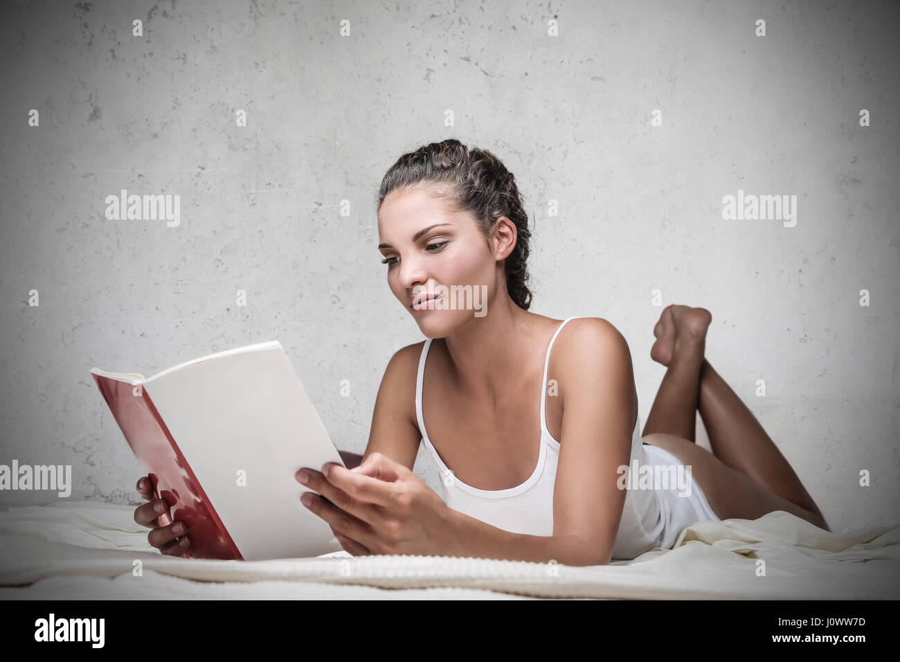 Brunette woman laying on bed, reading a book Stock Photo