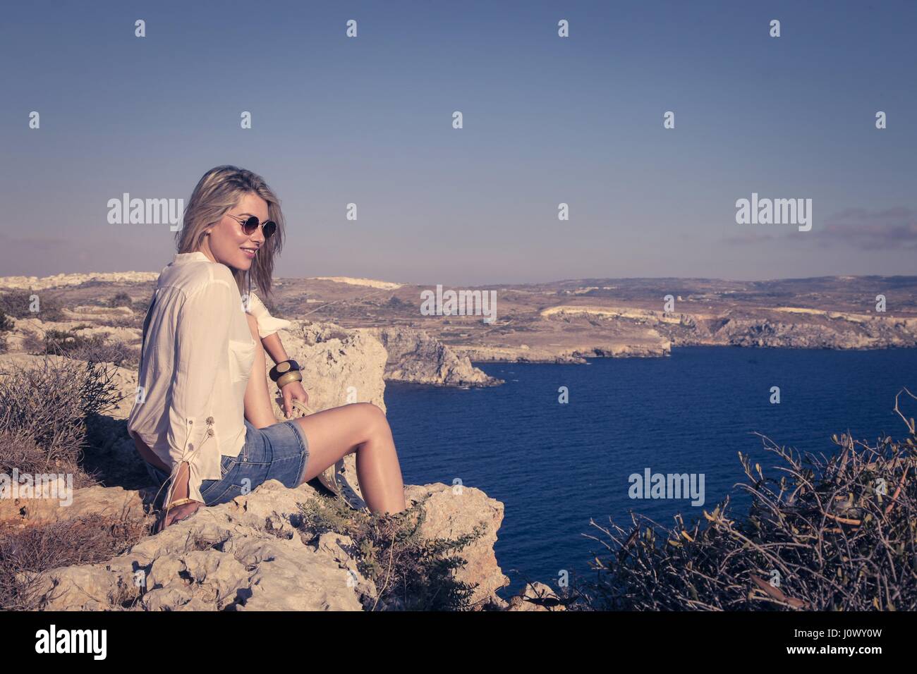 Blond woman sitting on cliff Stock Photo Alamy