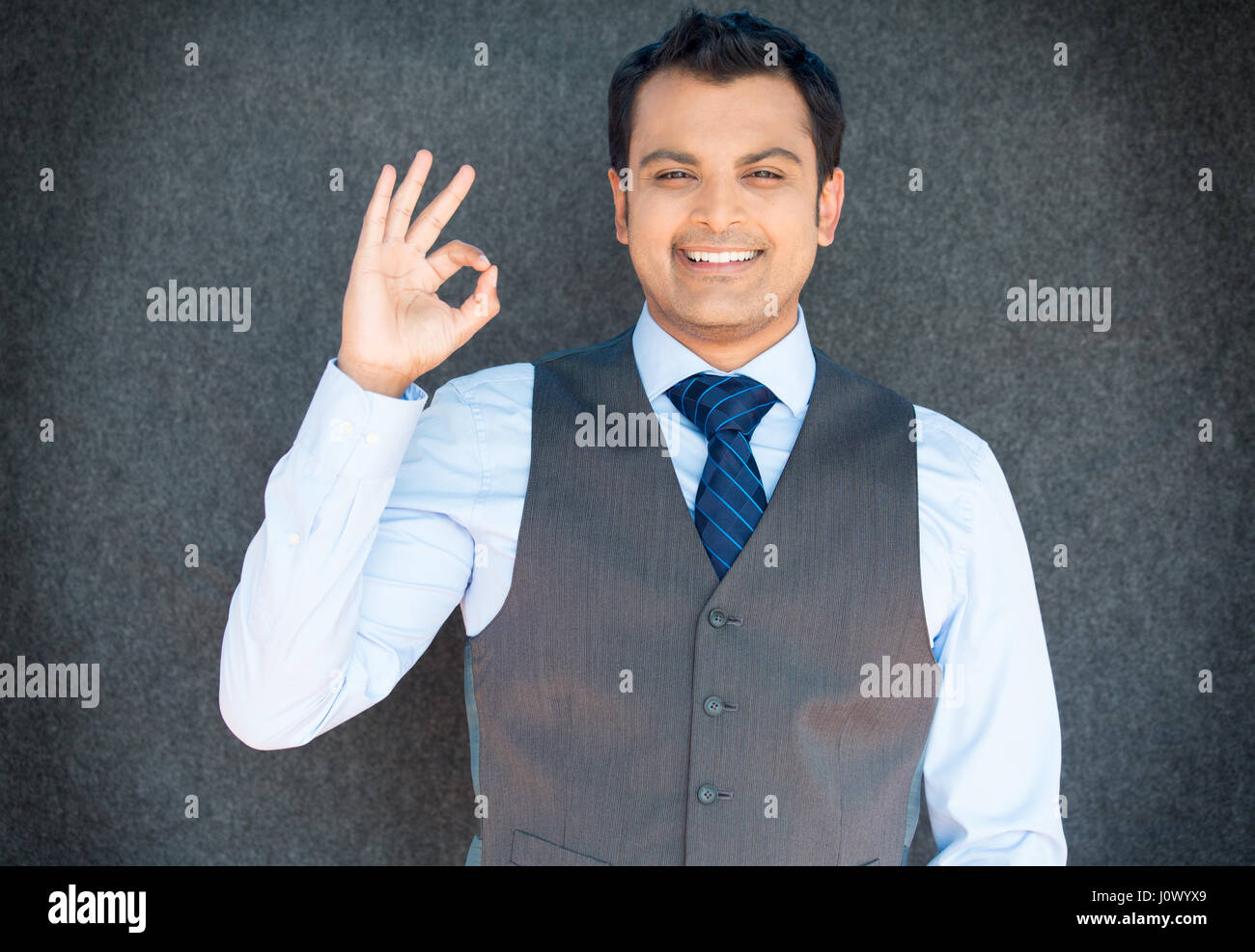 Closeup portrait of young handsome happy, smiling excited man giving OK sign with fingers, isolated gray background. Positive human emotions, facial e Stock Photo