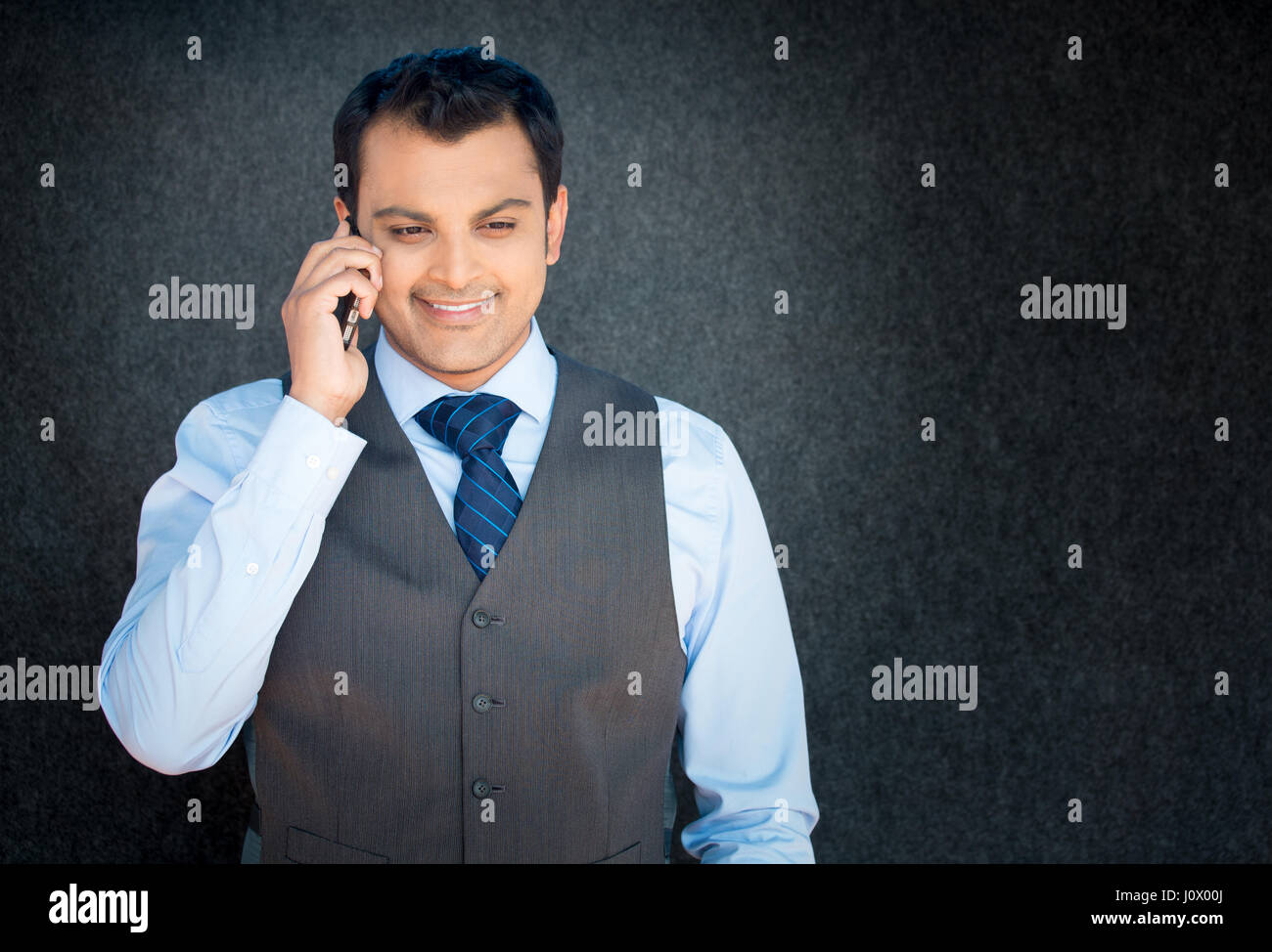 Closeup portrait, handsome young business man, happy guy, in vest and tie, using cell phone, smiling, having pleasant conversation, isolated gray blac Stock Photo
