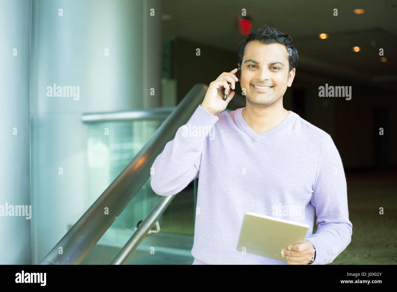Closeup portrait, handsome young business man, happy guy, in purple sweater, using cell phone and tablet, smiling, having pleasant conversation, isola Stock Photo