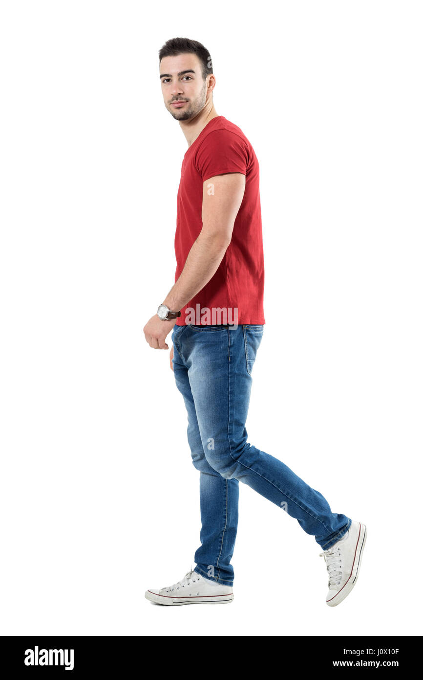 Side view of young relaxed casual man walking and looking at camera ...