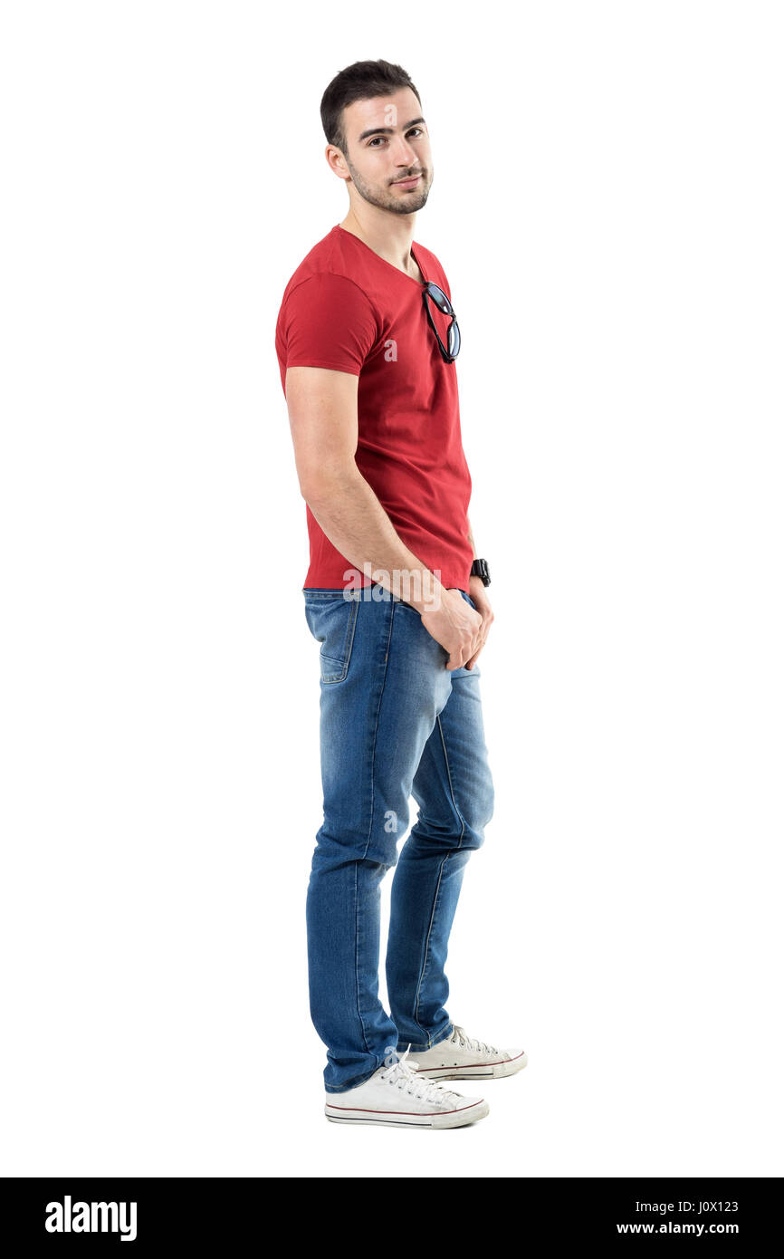 Side view of young relaxed casual man in red t-shirt and jeans looking at camera. Full body length portrait isolated over white studio background. Stock Photo
