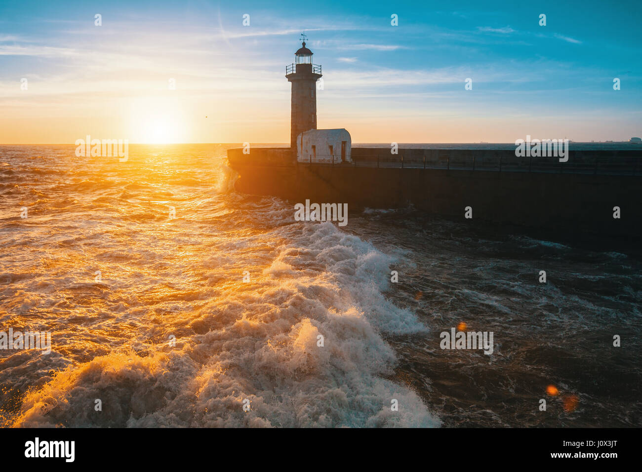 Beautiful sunset on the sea a stone pier and lighthouse. Atlantic coast in Portugal. Stock Photo