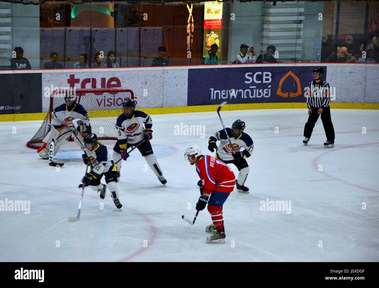 Malaysia team players defend goal vs Mongolia in Ice Hockey match in rink while referee watches Bangkok Thailand Stock Photo
