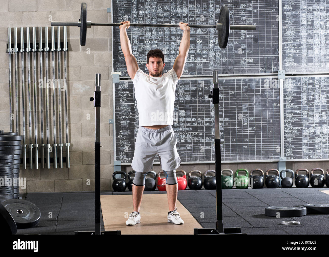 Full body view of young male bodybuilder lifting barbell above head ...