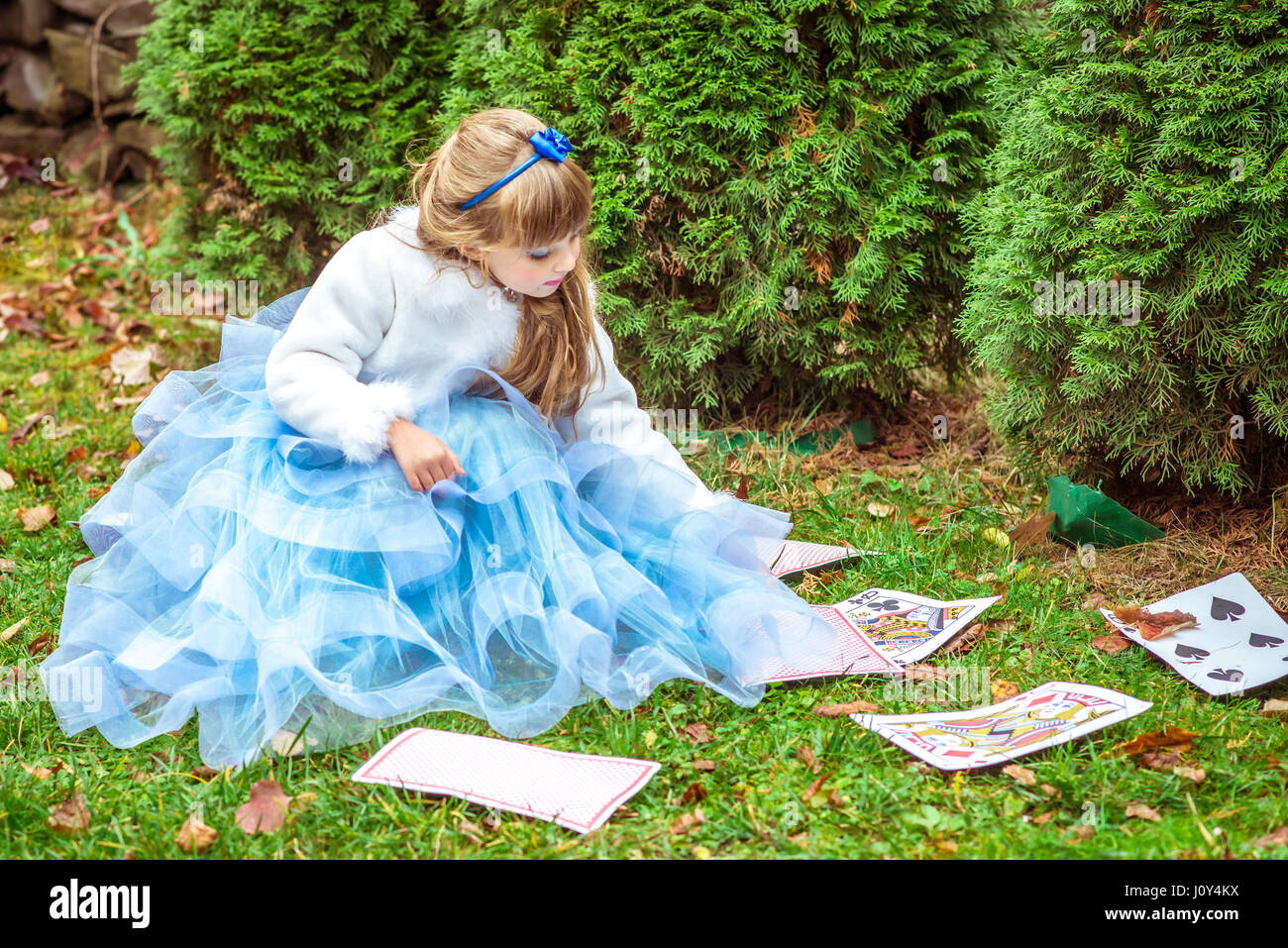 An little beautiful girl in a long blue dress sitting on the grass and ...