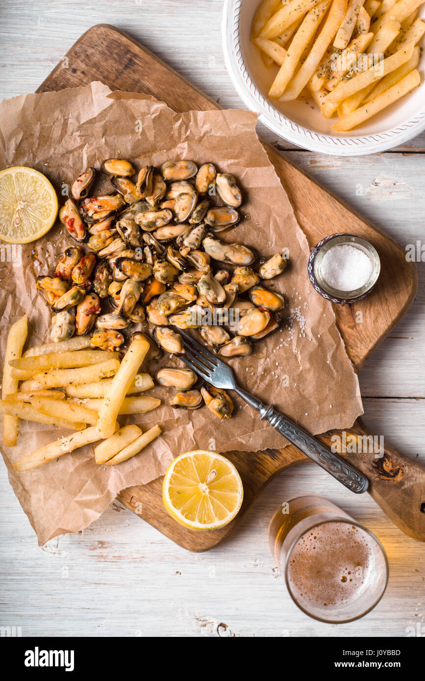 Mussels with lemons and French fries on the white wooden table vertical Stock Photo