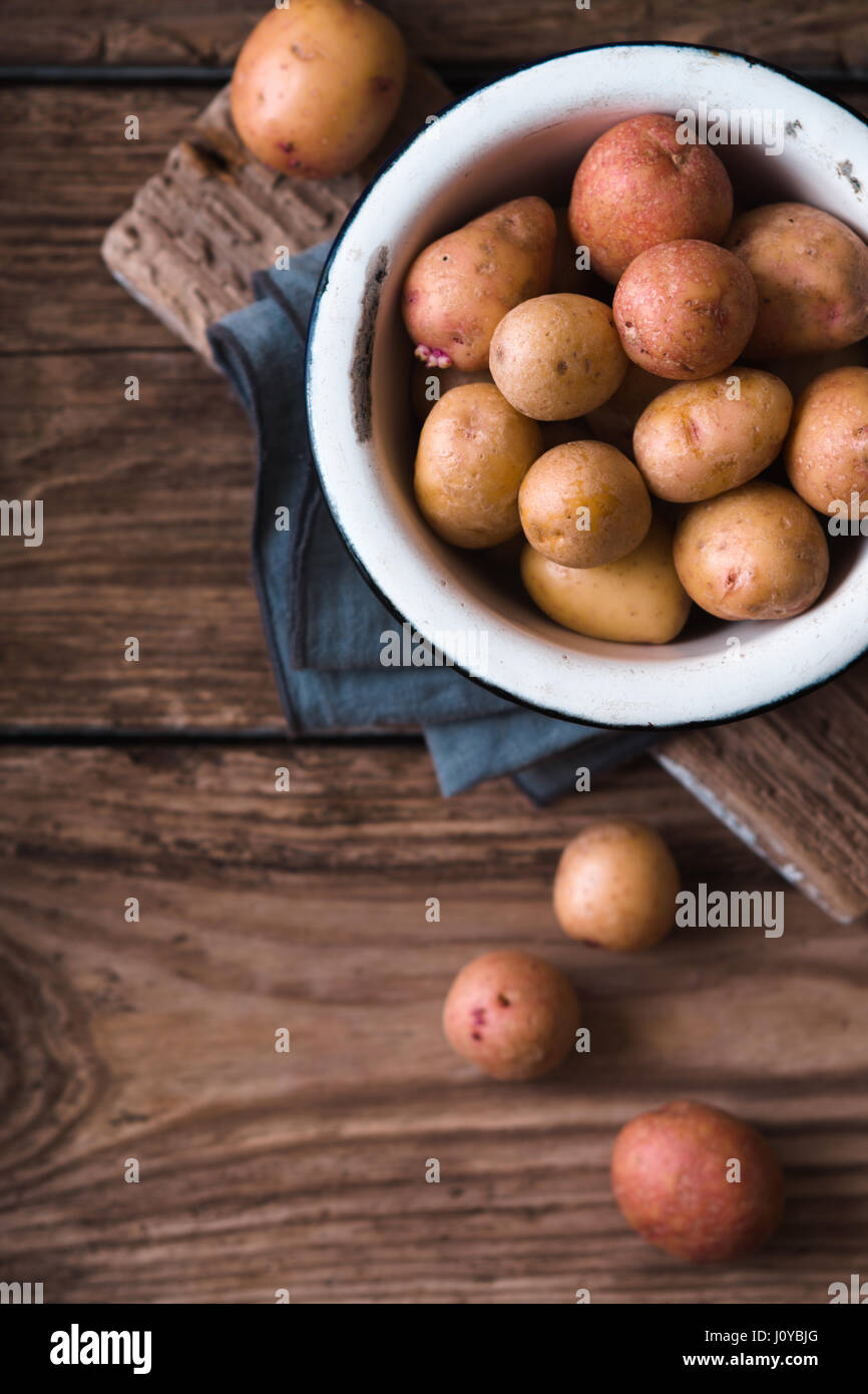 Raw potatoes in the metal bowl on the wooden table top view Stock Photo