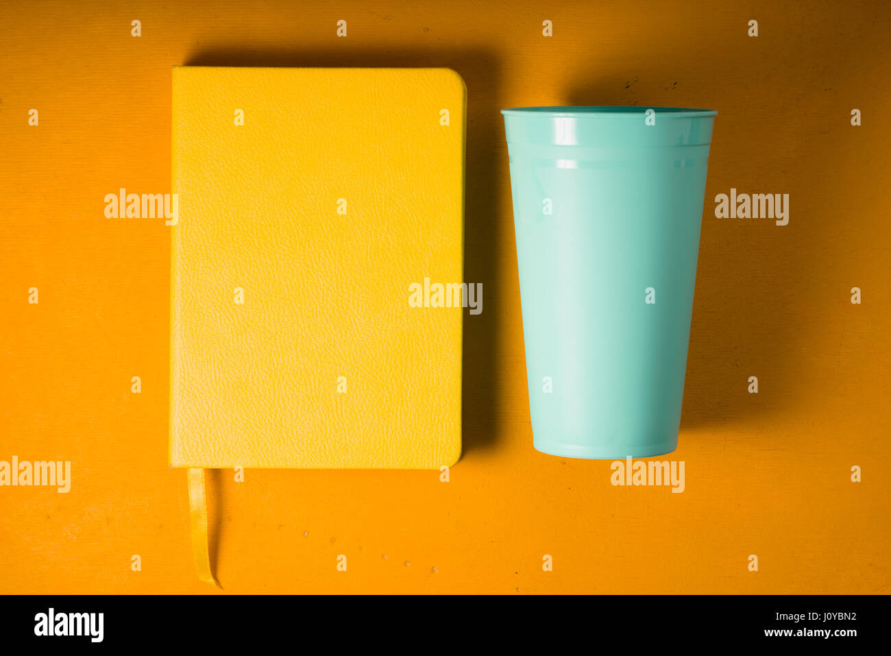 Notepad and plastic turquoise glass on a yellow background Stock Photo