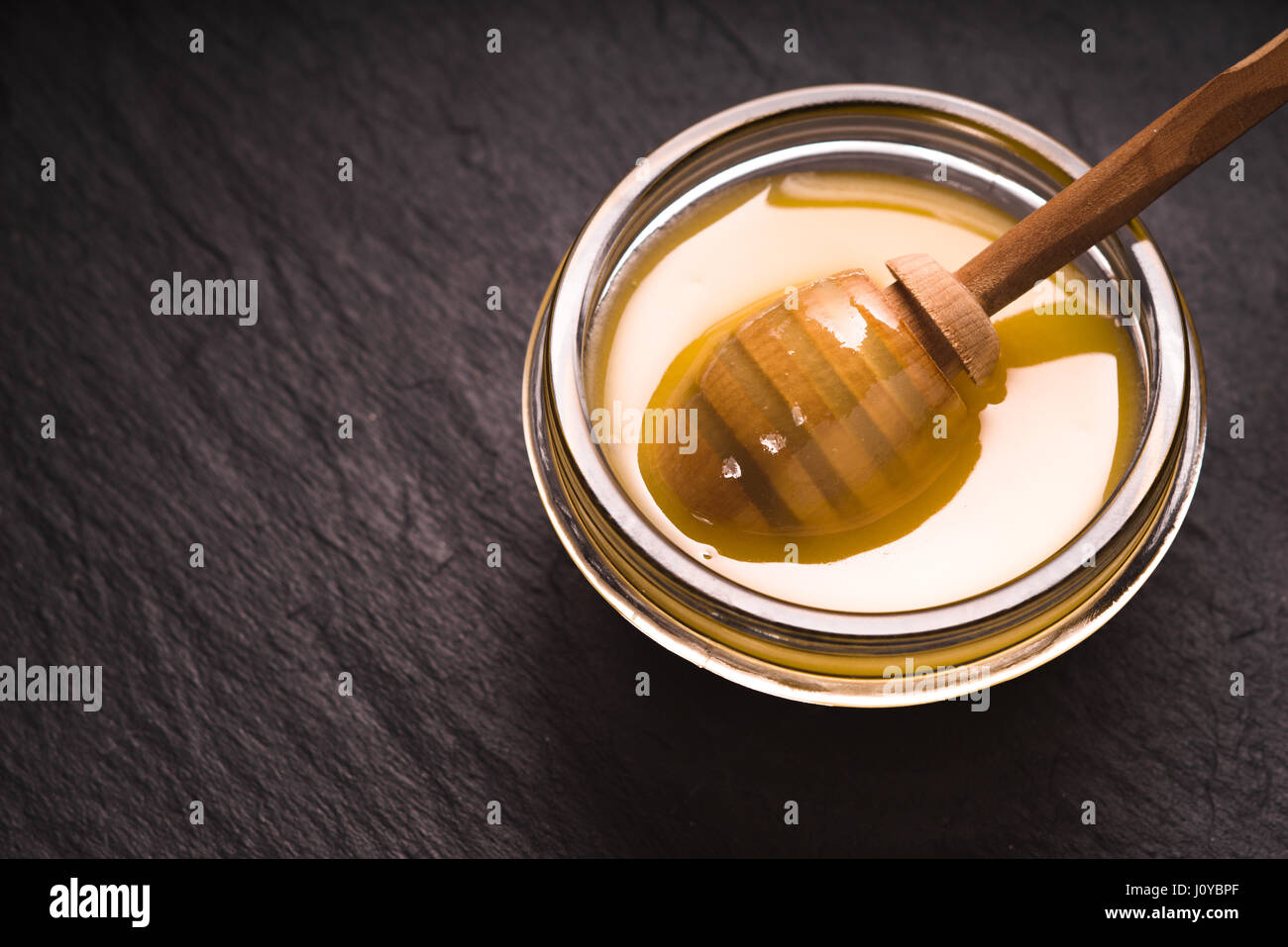 Spoon in a bowl of honey on a dark slate Stock Photo