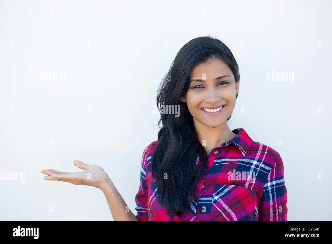 Closeup portrait happy confident young smiling woman gesturing, presenting space at left with palm up isolated white wall background. Positive human e Stock Photo