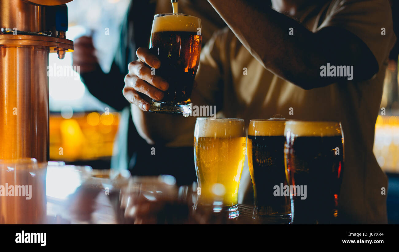 3 full pint glasses on a bar. 1 is being filled by a tap. Stock Photo