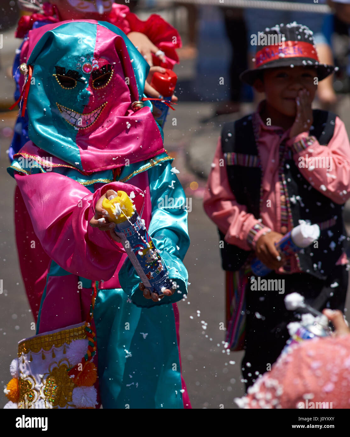 Child getting sprayed with foam by masked children at the annual Carnaval Andino con la Fuerza del Sol in Arica, Chile. Stock Photo