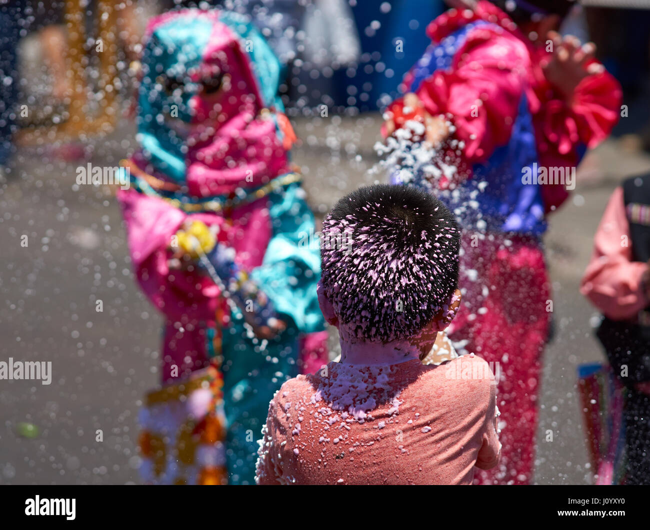 Child getting sprayed with foam by masked children at the annual Carnaval Andino con la Fuerza del Sol in Arica, Chile. Stock Photo