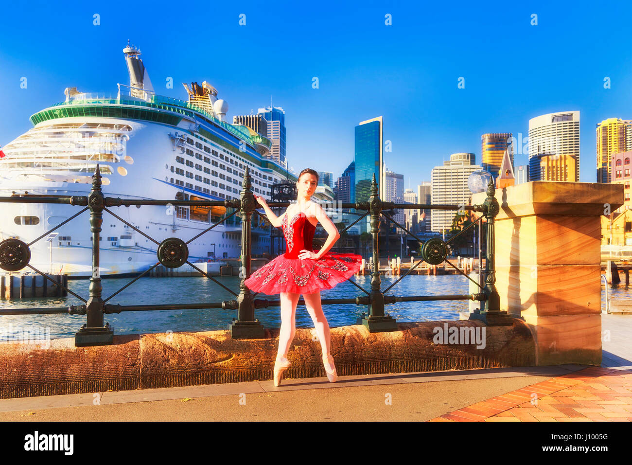 Ballerina in red concert tutu dressing point shoes standing on points at waterfront of Sydney harbour Stock Photo
