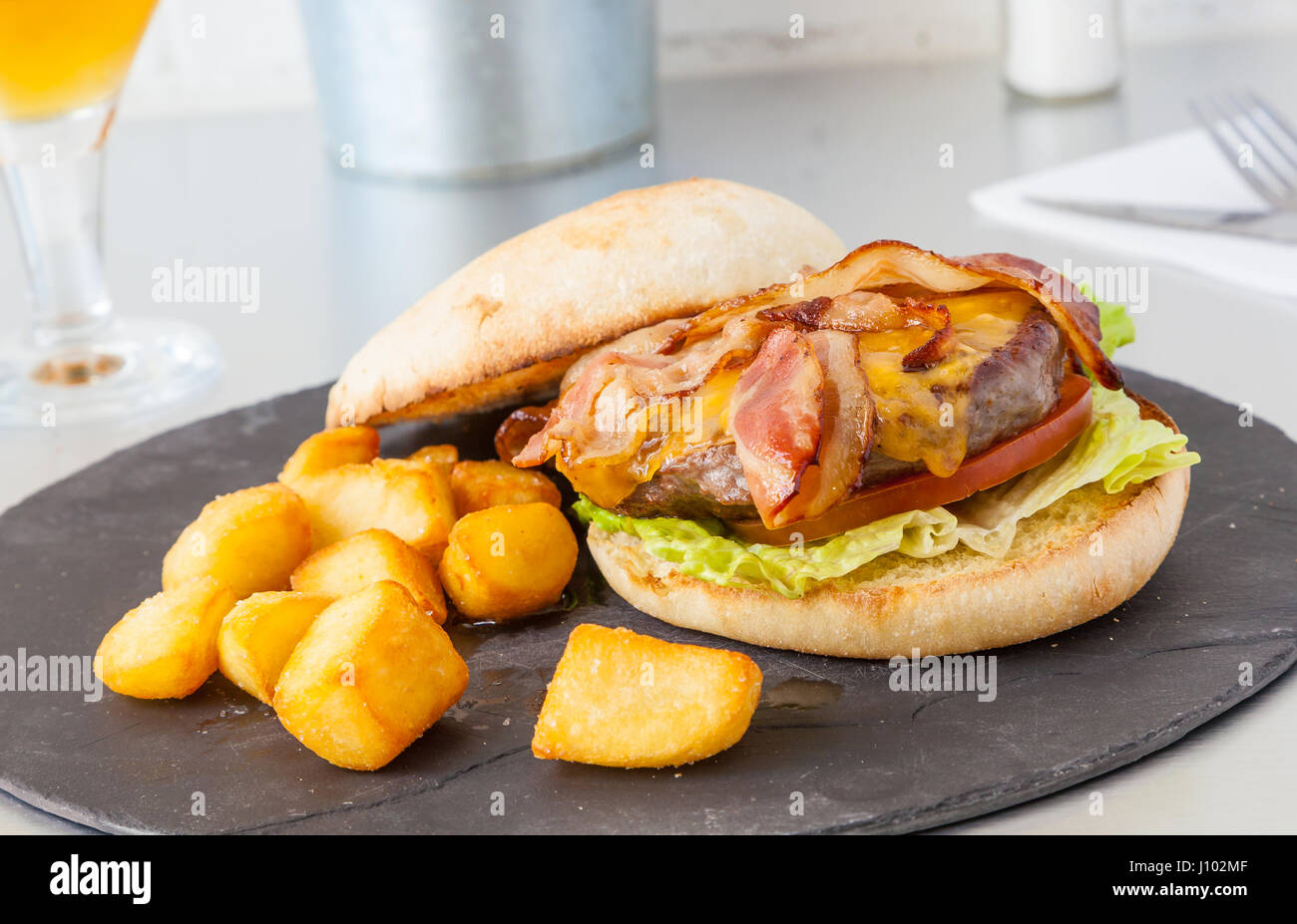Hamburger with cheese, bacon and fries on a black slate. Stock Photo