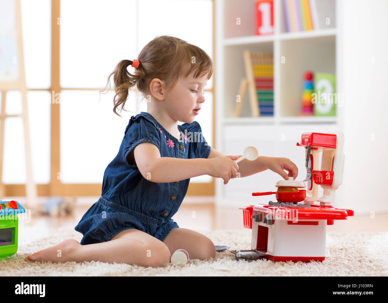 Pretty kid girl playing with a toy kitchen in children room or kindergarten Stock Photo