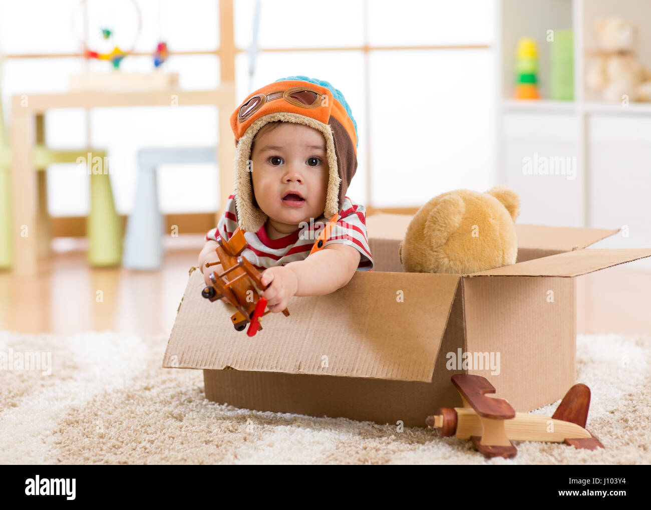 Pilot aviator baby boy with teddy bear toy and planes plays in cardboard box Stock Photo
