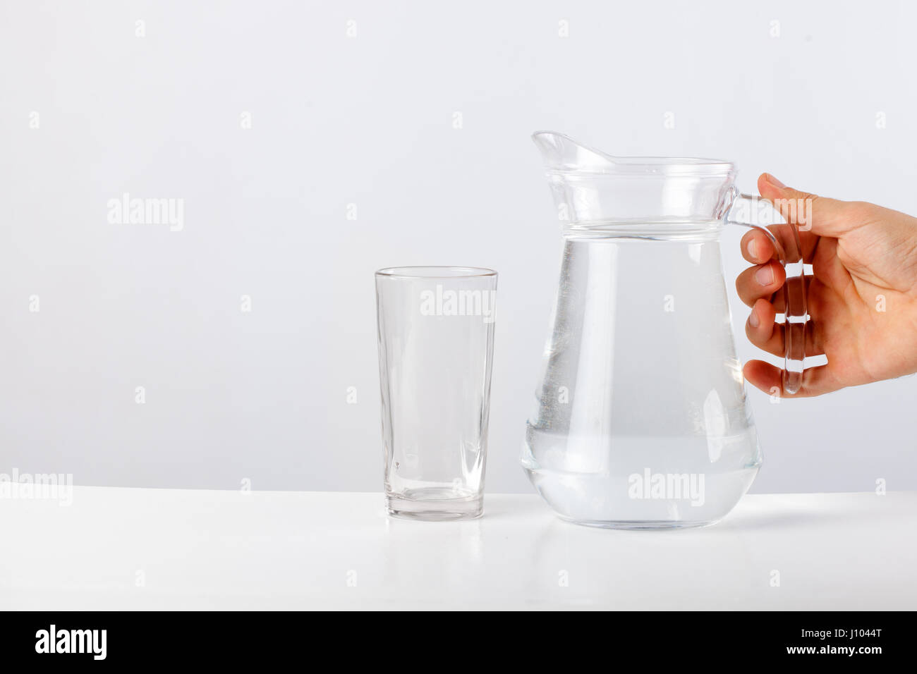 Hand pouring water from glass jug to glass against white background Stock Photo