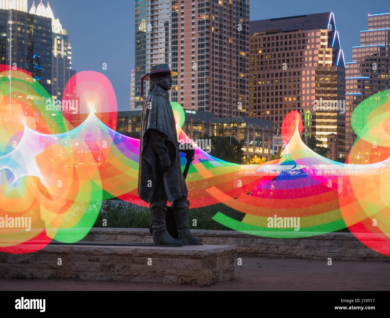 Stevie Ray Vaughan statue at night on Lady Bird Lake with a lighted rainbow in the background Stock Photo