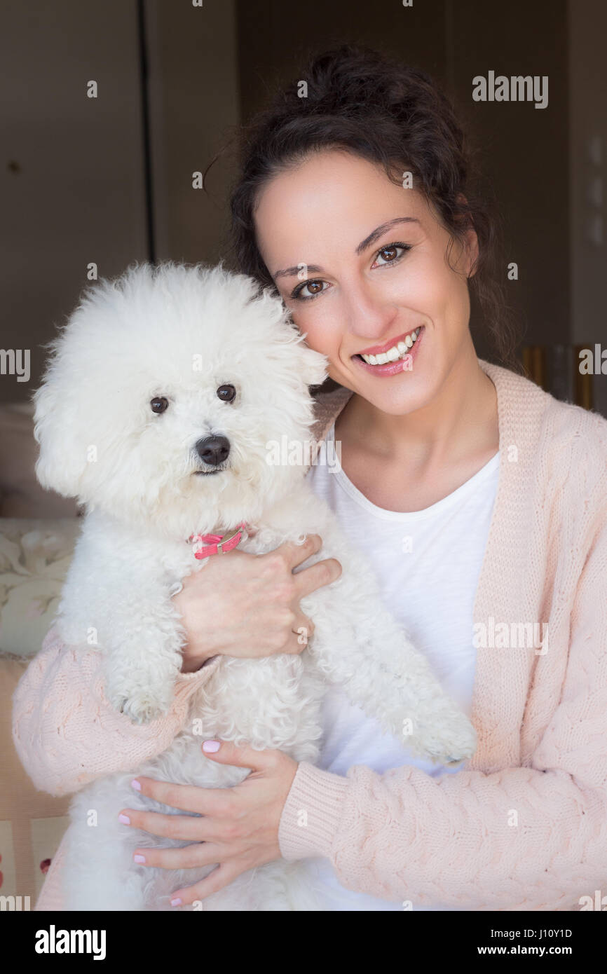 Portrait of a young woman holding her dog bichon frise at her home. Stock Photo