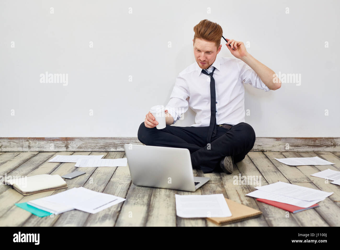 Portrait of modern young businessman sitting cross legged on floor in ...