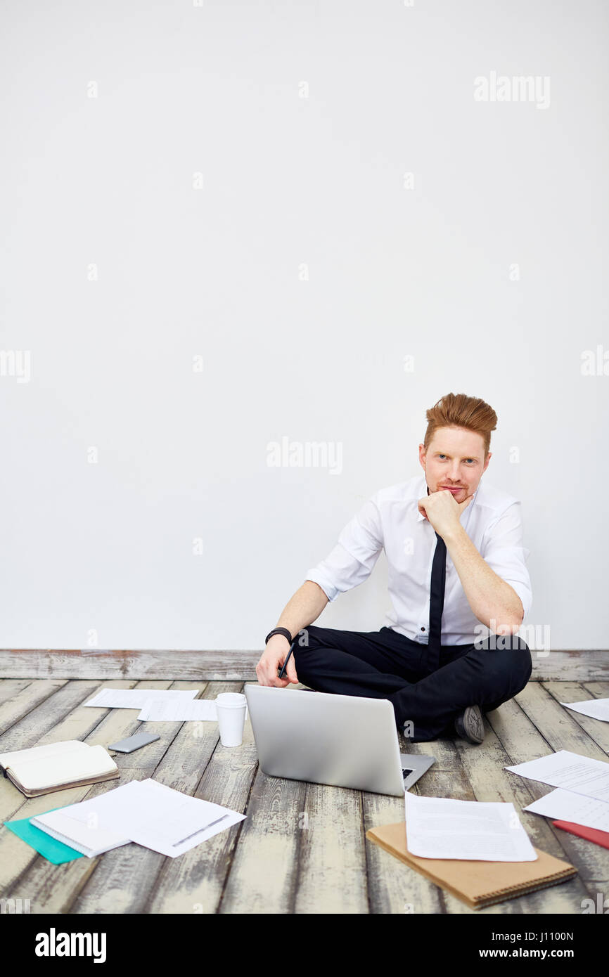 Portrait of modern young businessman sitting cross legged on floor in ...