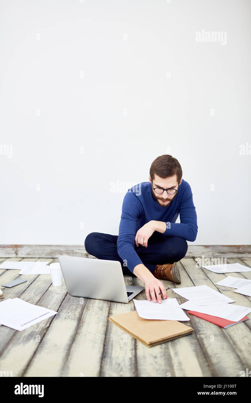 Portrait of bearded modern businessman sitting cross legged on floor in ...