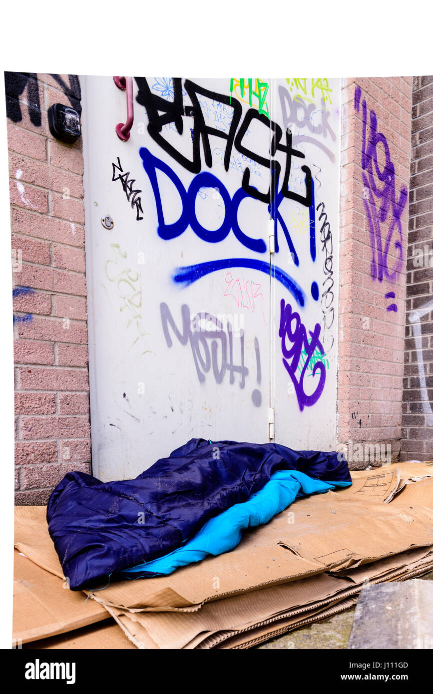 A sleeping bag and cardboard boxes on the ground in an alleyway behind an office block, used by a homeless person to sleep. Stock Photo