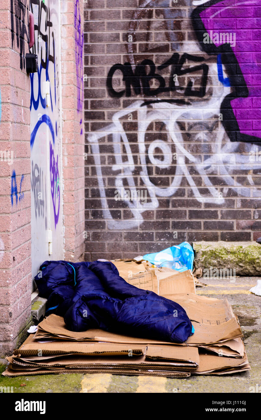 A sleeping bag and cardboard boxes on the ground in an alleyway behind an office block, used by a homeless person to sleep. Stock Photo