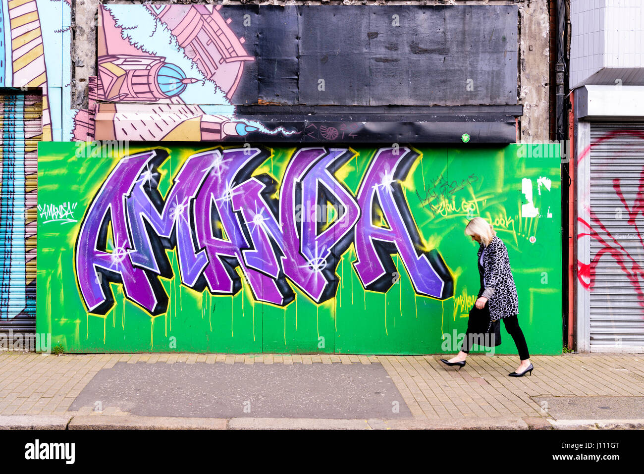 A woman walks past artistic graffiti of the girls name 'Amanda'. Stock Photo