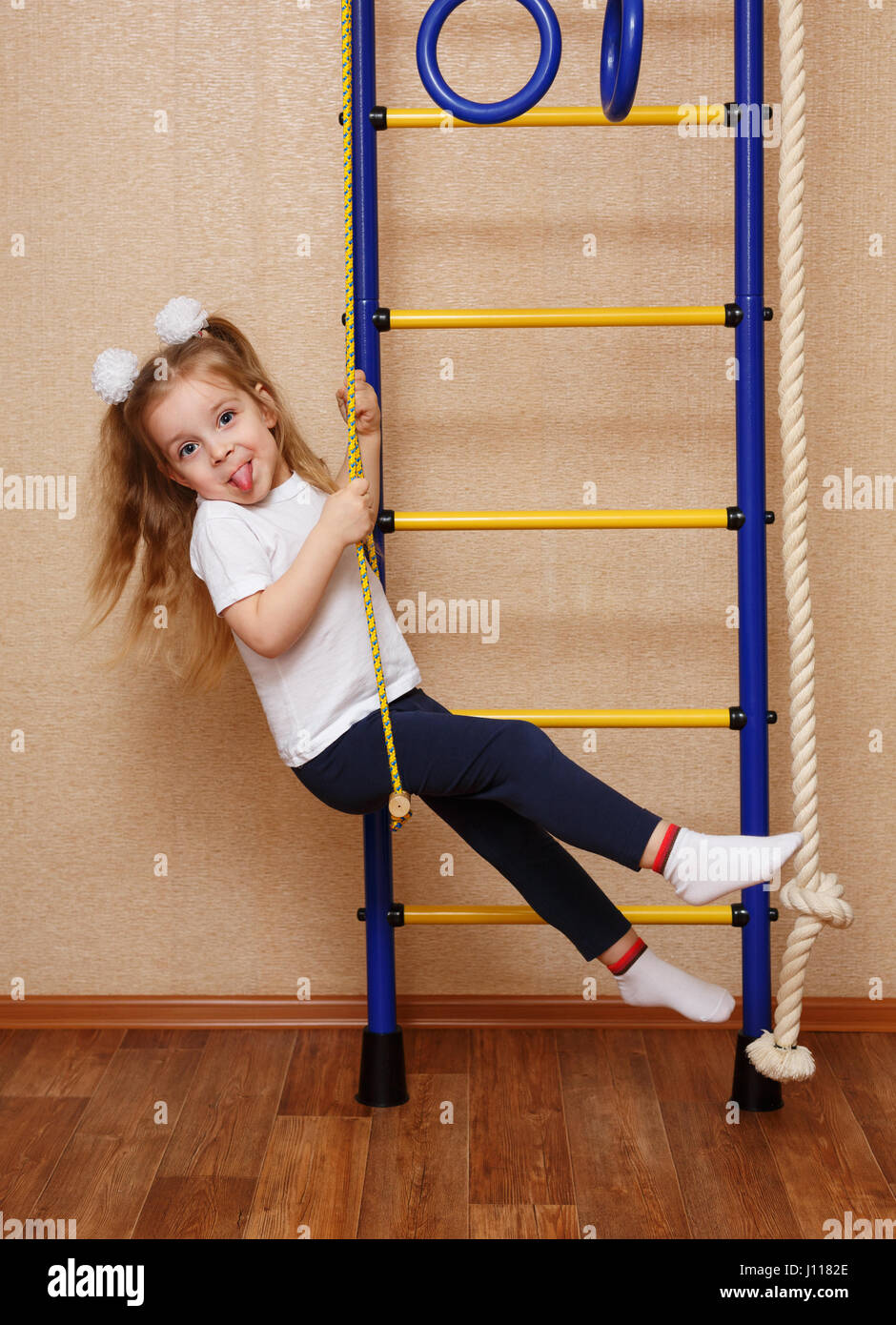 Little girl in sportswear showing tongue and riding on a swing on the wall bars. The concept of a healthy lifestyle from a young age. Children s sport Stock Photo Alamy