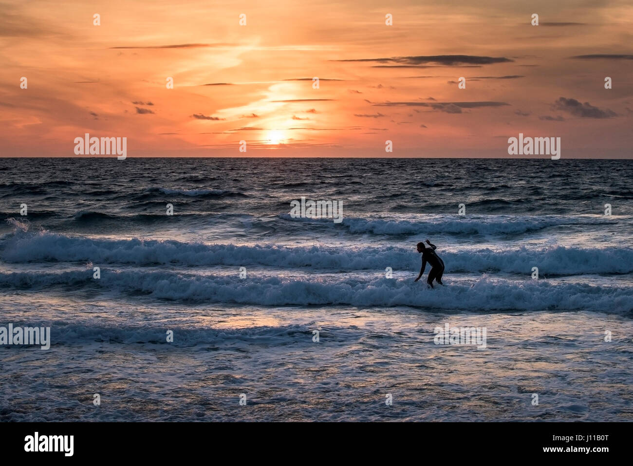 Surfing UK; Surfer; Sunset; Intense sunset; Evening; Fistral; Cornwall; Wave; Sea; Watersport; Physical activity; Skill; Leisure activity; Lifestyle;  Stock Photo
