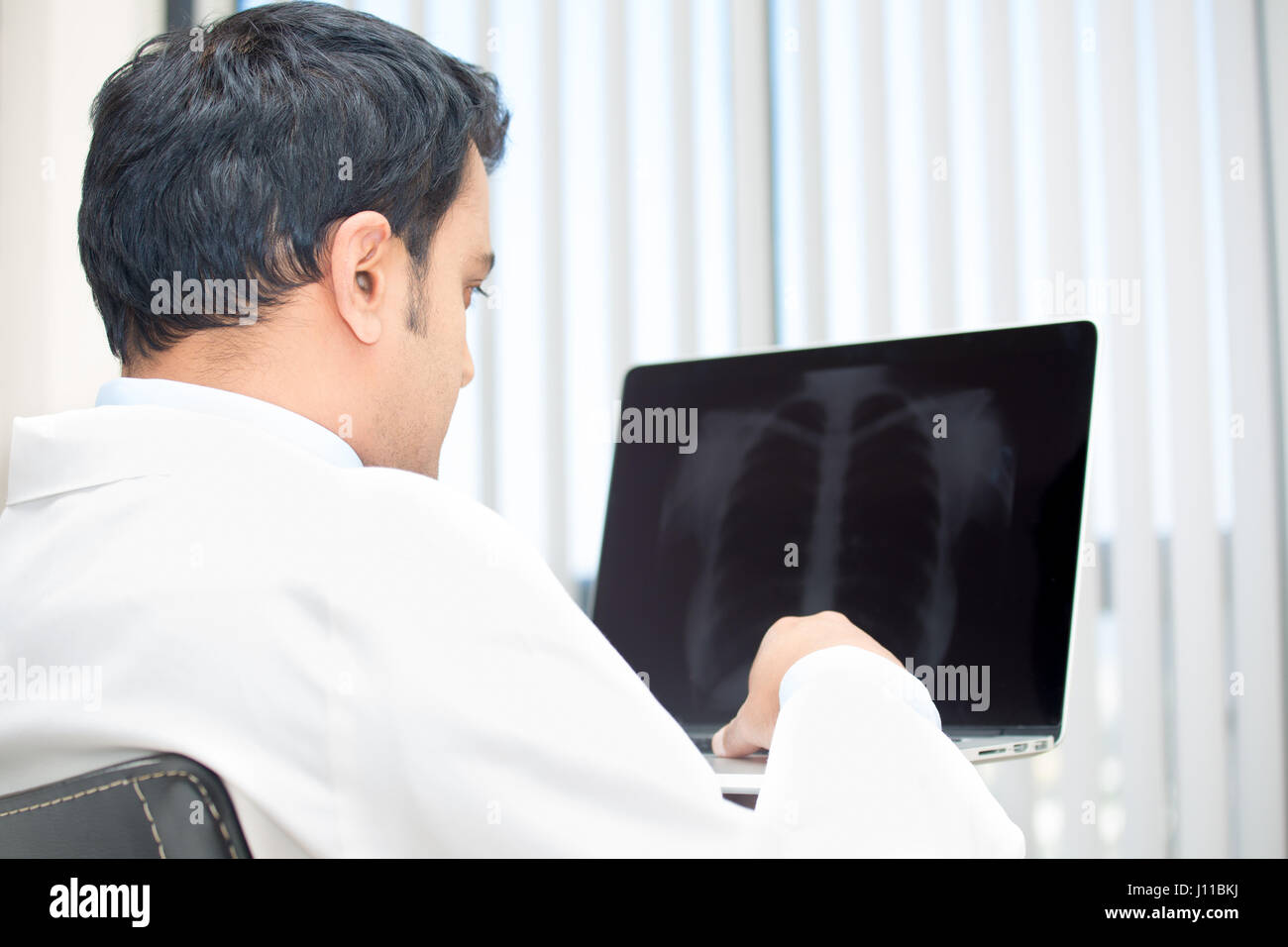 Closeup portrait of intellectual man healthcare personnel with white labcoat, looking at chest x-ray radiographic image, on laptop isolated hospital c Stock Photo