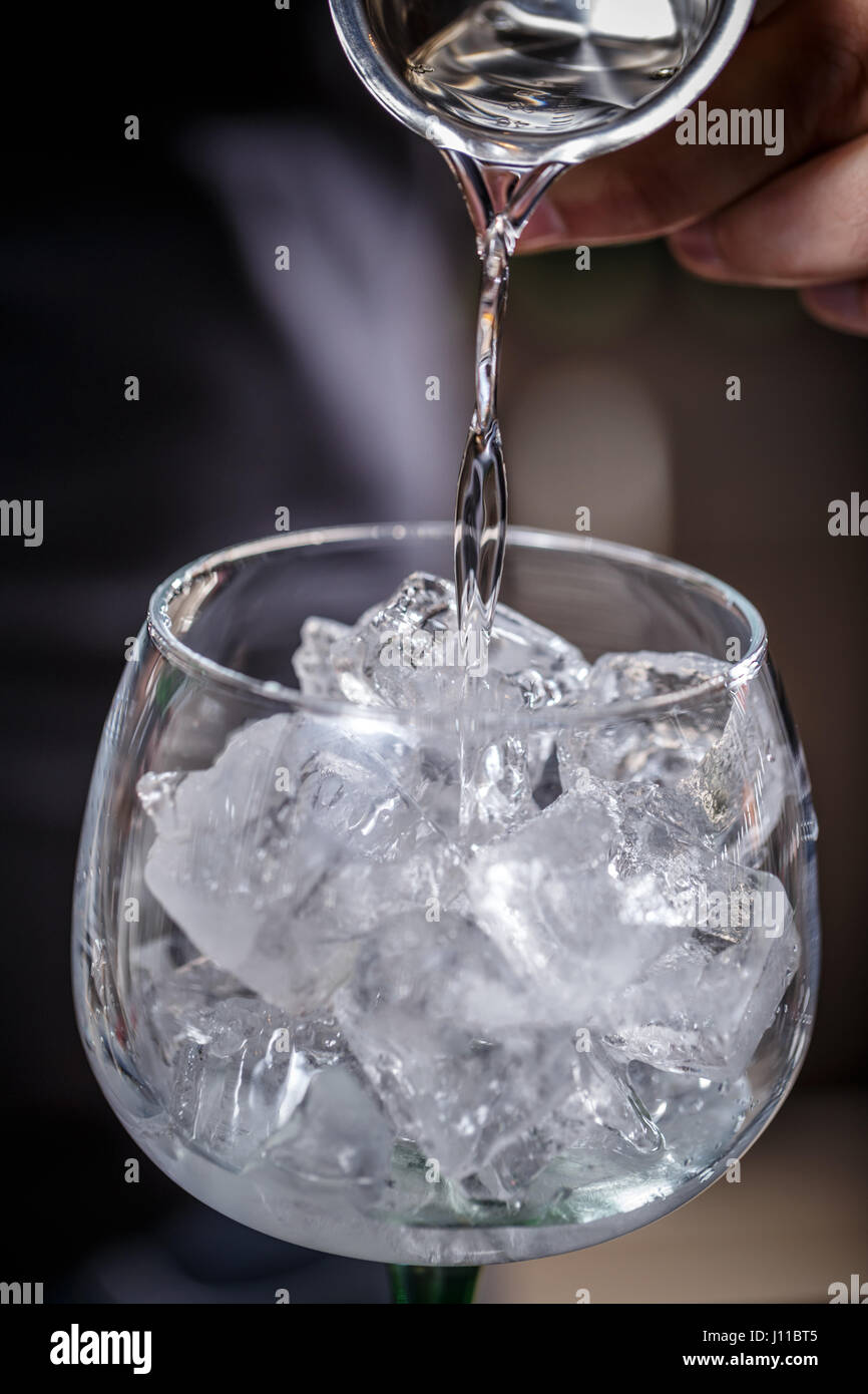 Barman is pouring alcohol from a jigger into a glass over ice; preparing an alcoholic cocktails Stock Photo