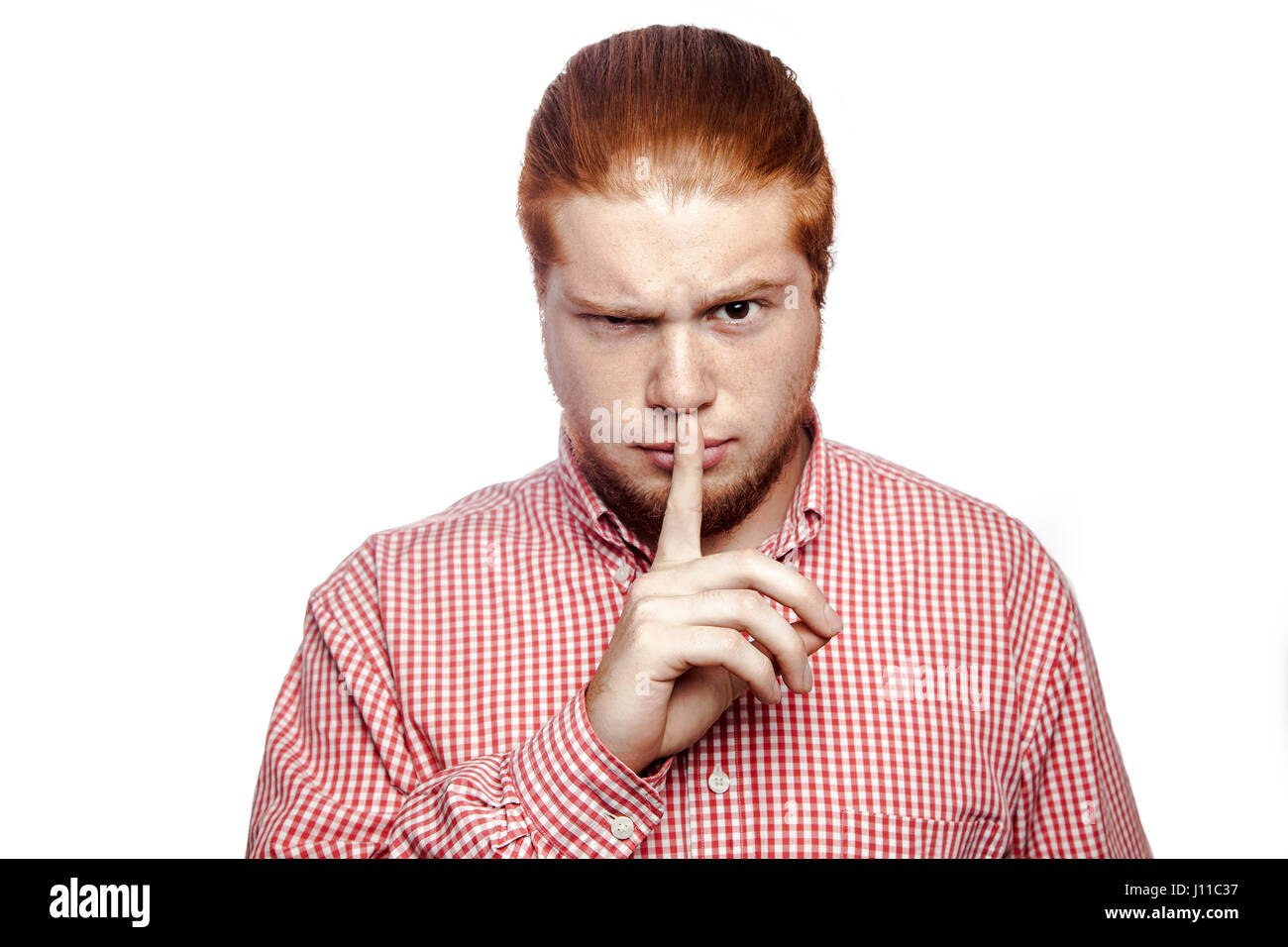 Serious businessman with finger on lips making silence gesture. shhh! bearded readhead businessman with red shirt and freckles looking at camera. stud Stock Photo