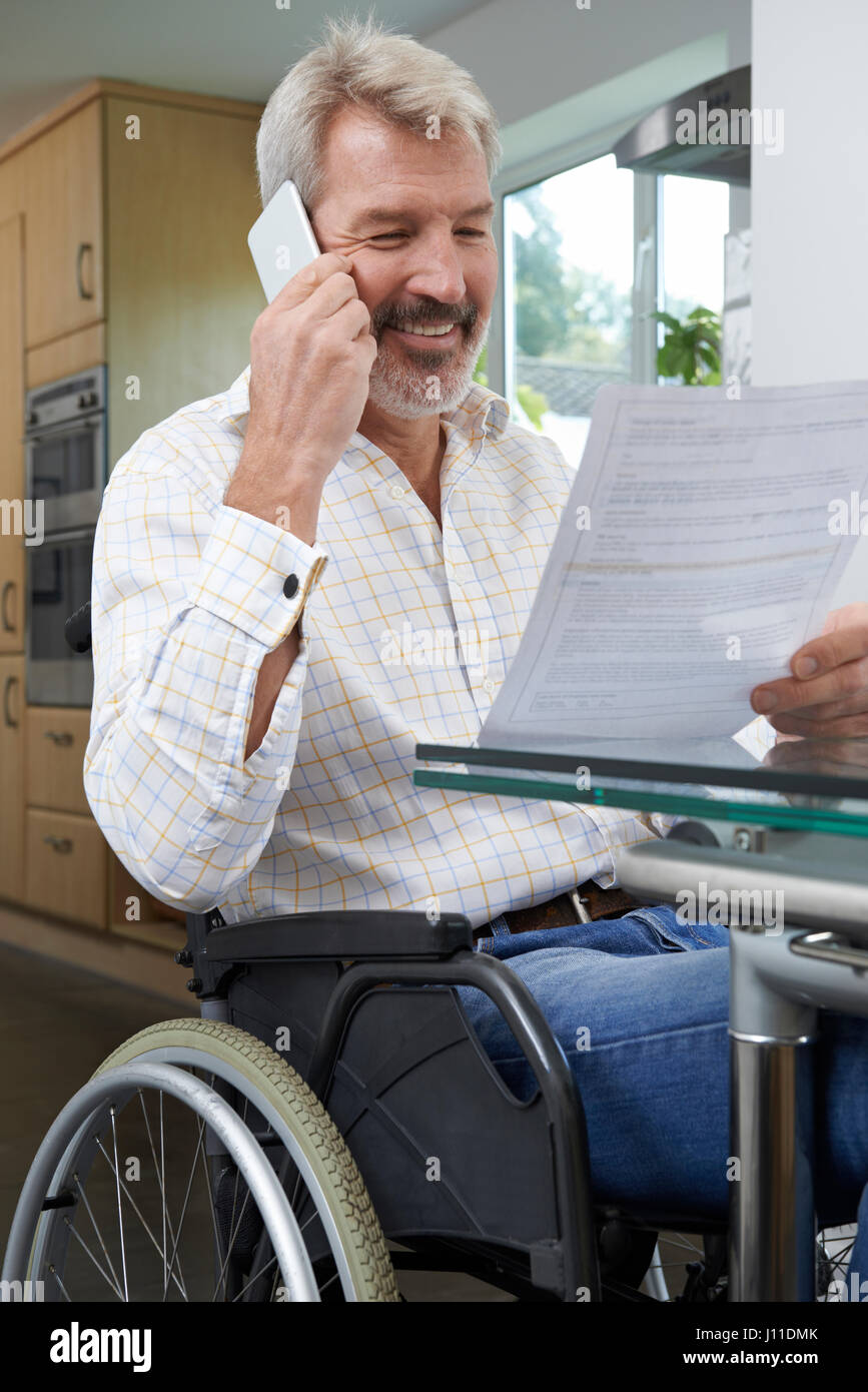 Man In Wheelchair Making Phone Call Whilst Reading Letter Stock Photo