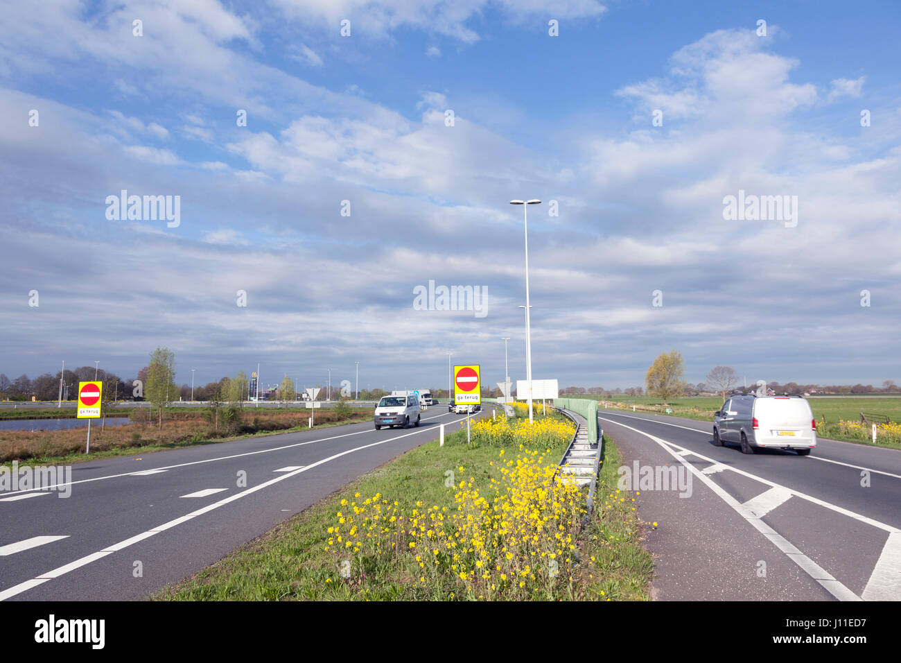 ramp to motorway A12 at dutch town Veenendaal with traffic ans yellow rapeseed flowers in spring Stock Photo