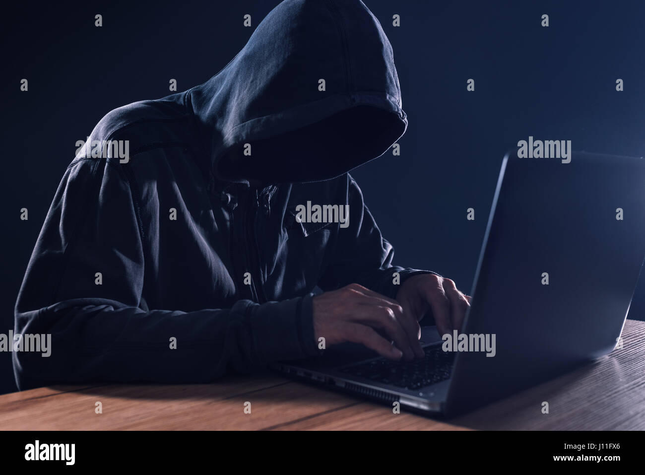 Cyber crime and computer virus concept with hooded faceless person working on laptop Stock Photo