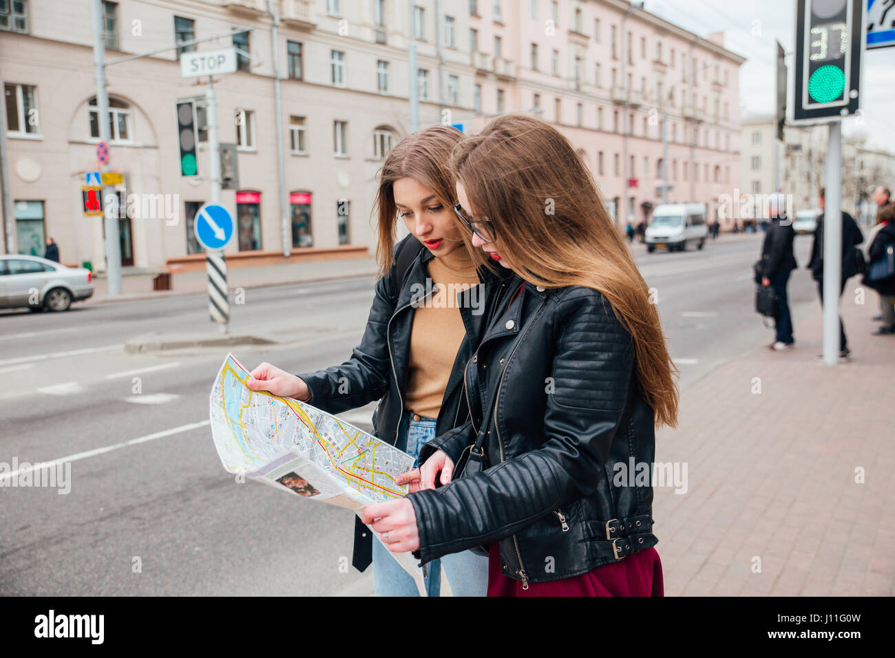 Two young stylish women traveling and looking at the map in city Stock Photo