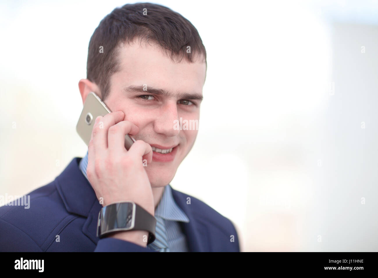 Good business talk. Handsome young man in formalwear talking on the phone and smiling while sitting at the office desk Stock Photo
