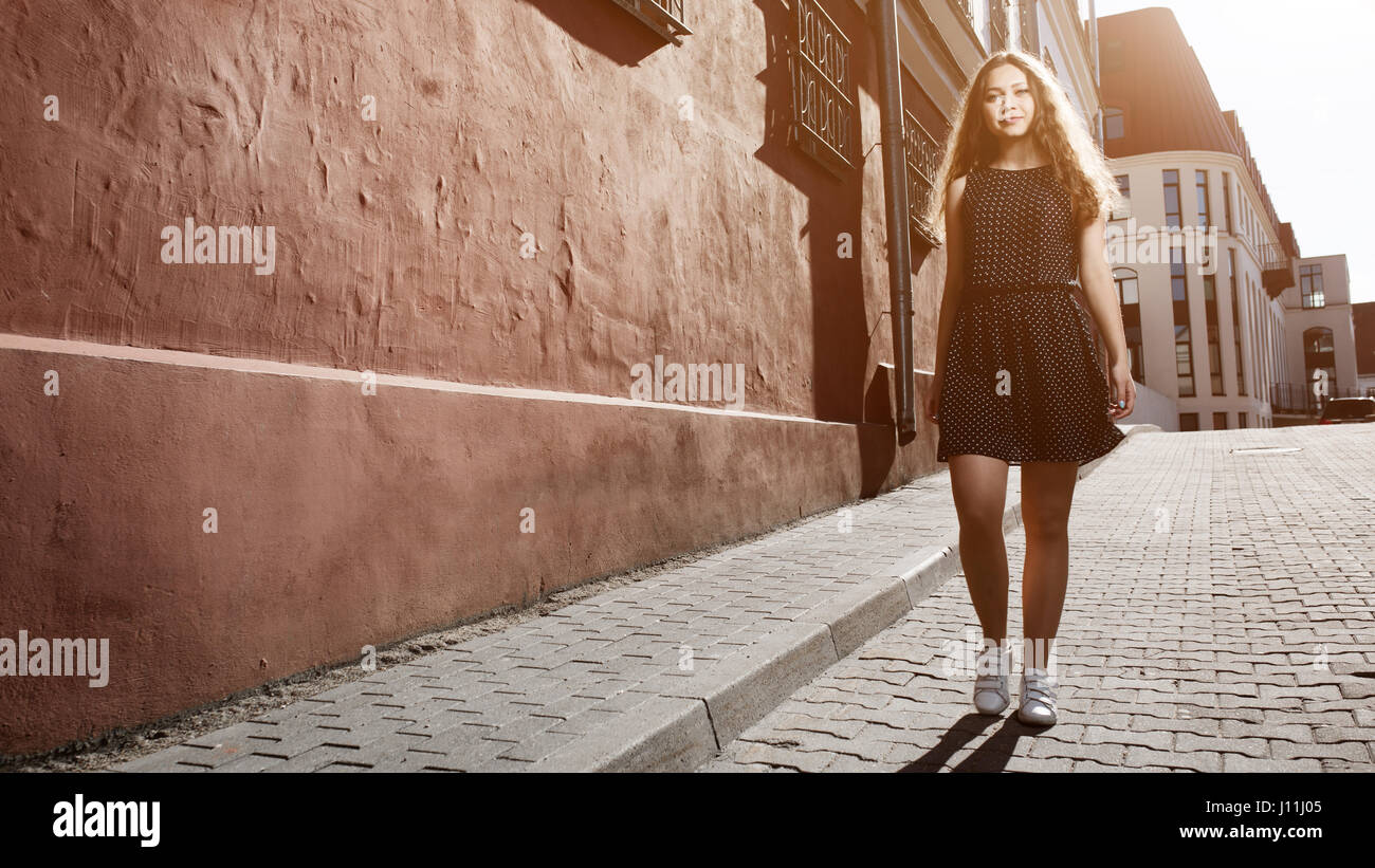 Beautiful brunette young woman wearing dress and walking on the street ...