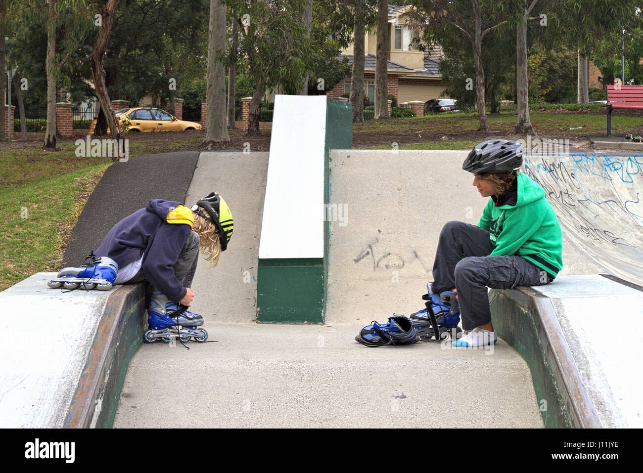 Boys Ramp Two boys sitting on a skate ramp doing up their inline skates or roller ...