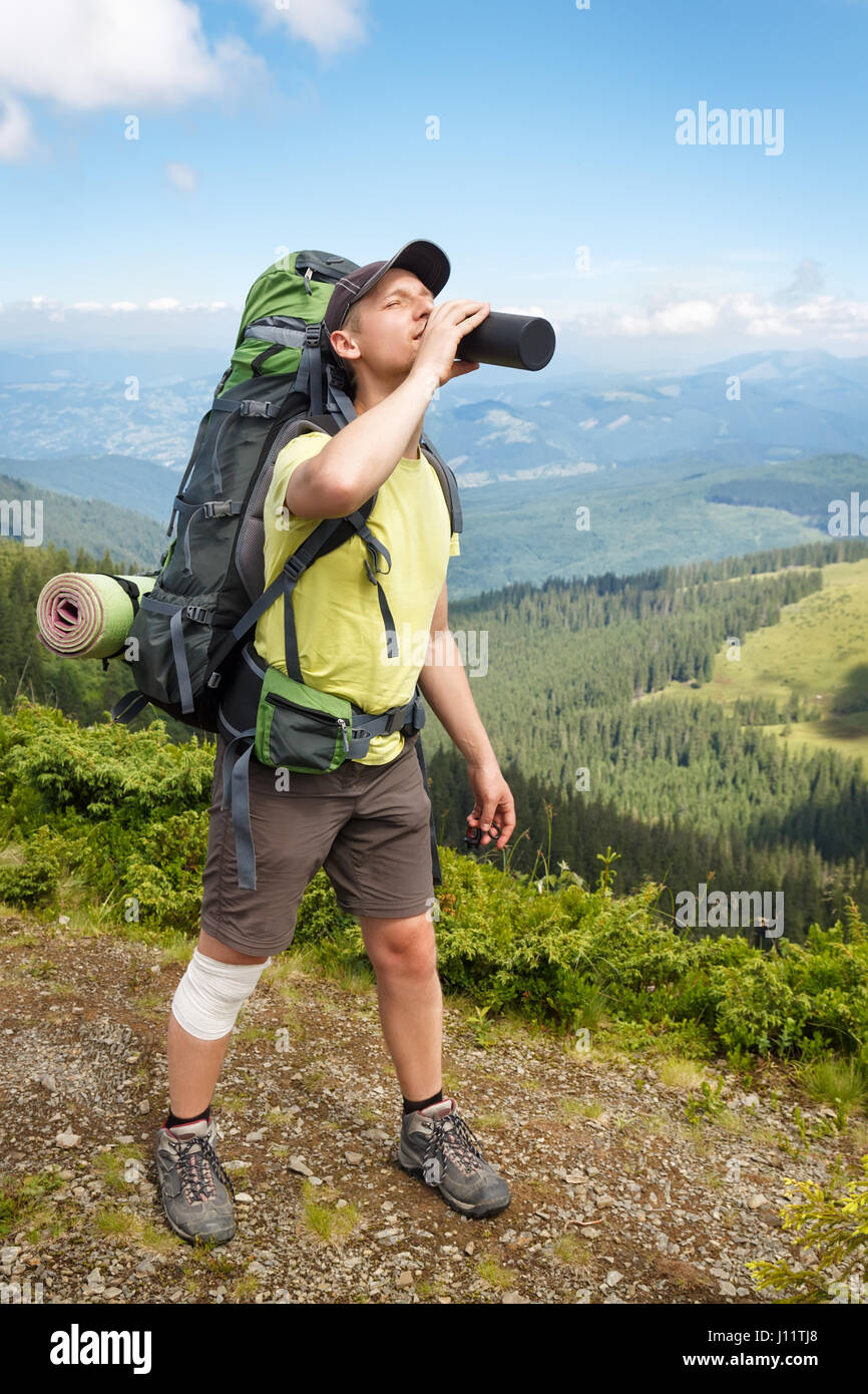 hiker in the mountains drinking water from his water bottle. Caucasian male tourist drinks water. Healthy lifestyle, adventure, tourism and hiking tri Stock Photo