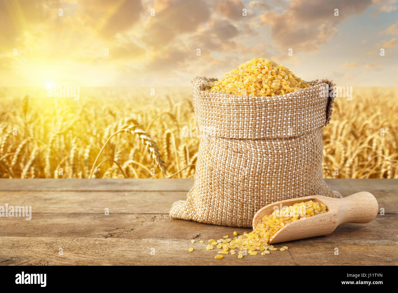 uncooked bulgur or couscous grains in sack on table with ripe field on