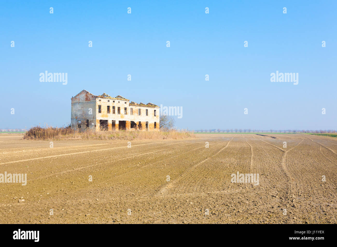 Rural Italian landscape from Po river lagoon.Plowed fields with perspective lines. Abandoned warehouse Stock Photo