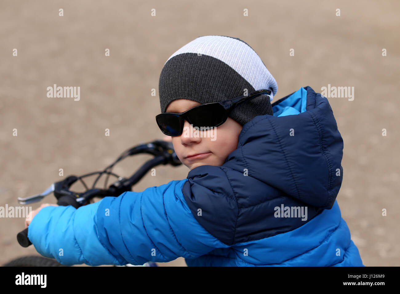 A boy wearing sunglasses sits on a bicycle. Stock Photo