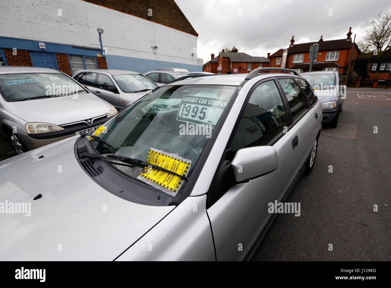 Cars for sale at an off-street lot parked on the public highway with parking tickets due to the double yellows on Hainault Avenue, Westcliff on Sea Stock Photo